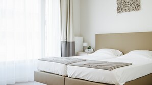 A modern hotel room with a large bed, a bedside table with a lamp, and a view of the outdoors through sheer curtains. - Domitys Emerald Haven (Antwerp)