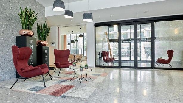 A modern lobby with red chairs, a coffee table, and potted plants. - Domitys Emerald Haven (Antwerp)