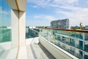 A modern balcony with glass railings, a white spherical object, and a view of a multi-story building in the background. - Domitys Emerald Haven (Antwerp)