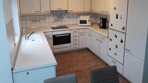 A compact kitchen with white cabinets, a microwave, a coffee maker, and a refrigerator with fruit magnets.