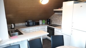 A compact kitchen with a sink, stove, microwave, and refrigerator. There is a dining table with chairs.
