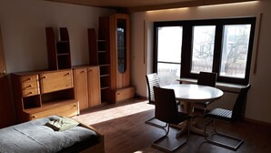 A room with a bed, a desk, a chair, a table, and a window with a view of buildings.