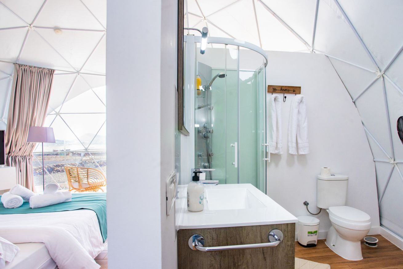 Une salle de bain moderne aux motifs géométriques, dotée d’une douche à parois de verre, d’un lavabo blanc et de toilettes.