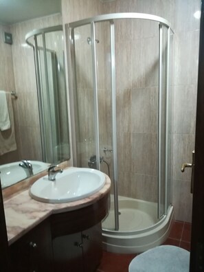 A bathroom with a glass-enclosed shower, a sink with a marble countertop, and a mirror. - Portfólio Guesthouse (Porto)