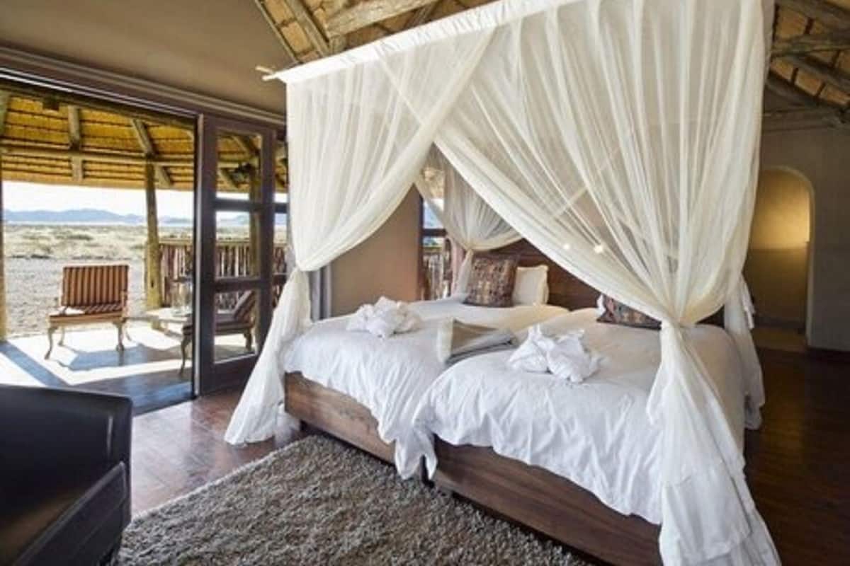 A bedroom with a four-poster bed, white linens, and a view of the beach through large glass doors.
