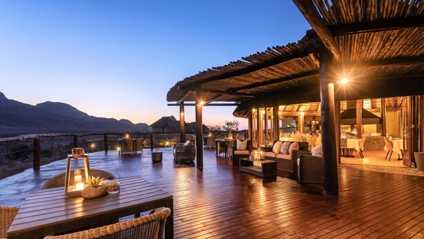 A wooden deck with outdoor seating, a dining area, and a view of the mountains. - Hoodia Desert Lodge (Sesriem)