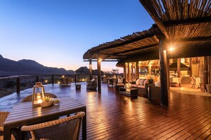 Una terraza de madera con asientos exteriores, un comedor y vistas a las montañas.