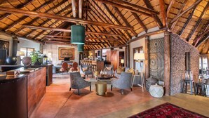 A spacious lobby with a high wooden ceiling, comfortable seating, and a decorative wall. - Hoodia Desert Lodge (Sesriem)