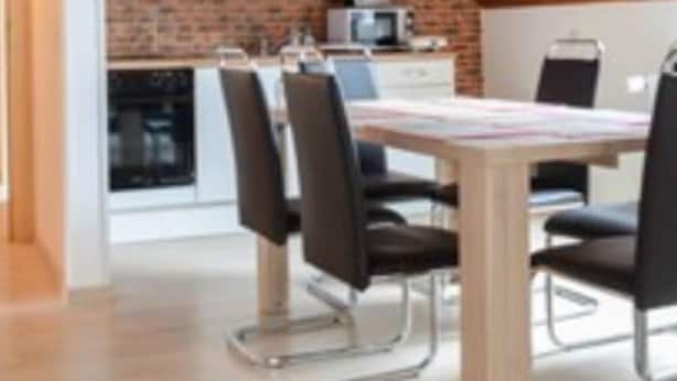 A dining area with a wooden ceiling, a brick wall, and a white kitchen in the background. - Monteurzimmer & FeWo G. Klement Aurach (Herrieden)