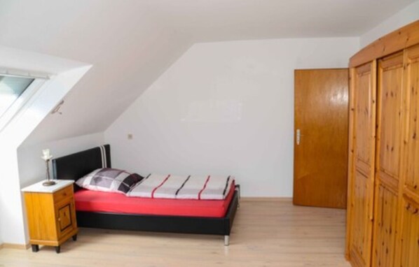 A bedroom with a bed, a nightstand, a wardrobe, and a skylight.