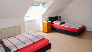 A bedroom with two beds, a skylight, a nightstand, and a radiator. - Monteurzimmer & FeWo G. Klement Aurach (Herrieden)
