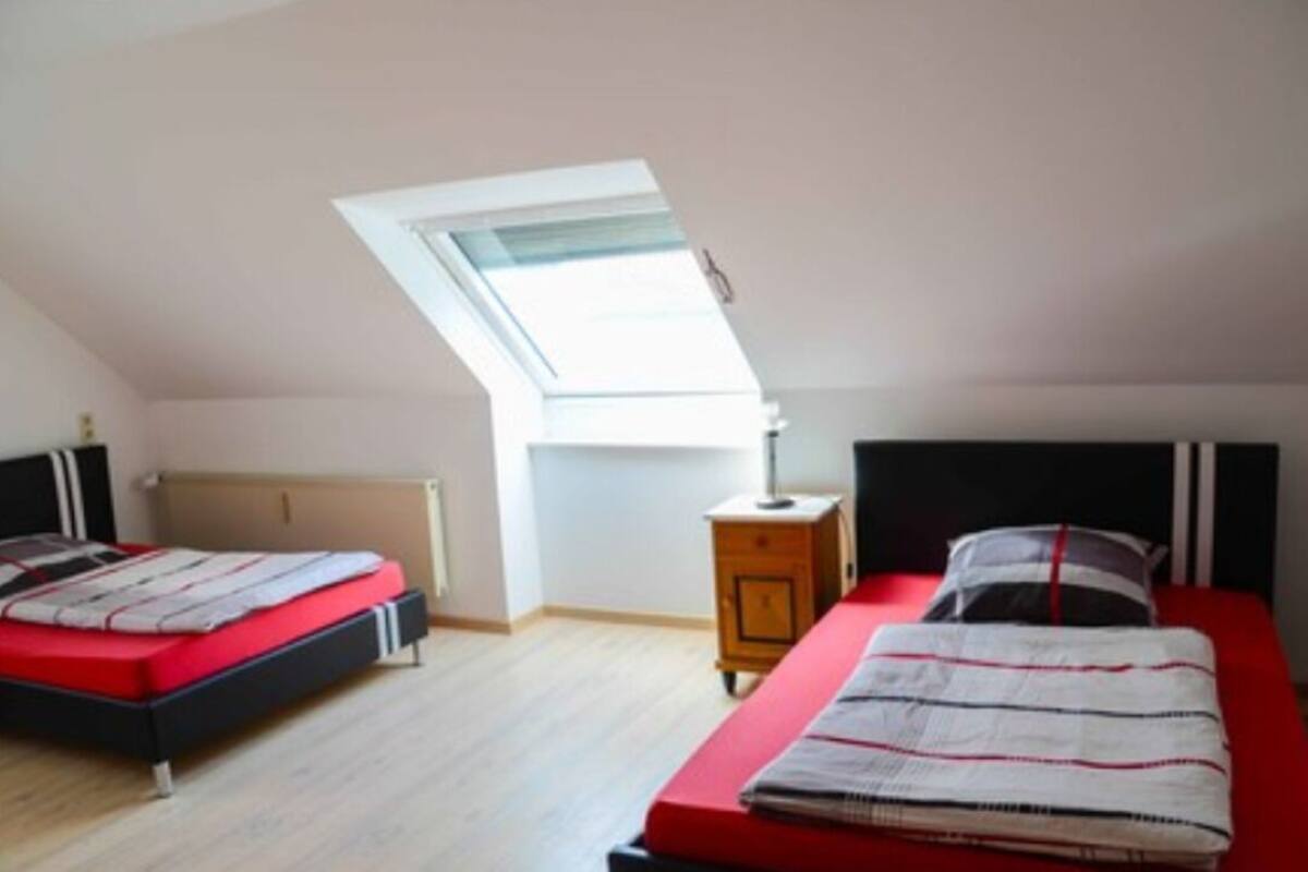 A bedroom with two beds, a skylight, a bedside table, and a radiator.