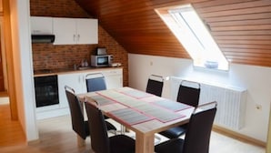 A dining area with a table set for four, a kitchen with a microwave, and a sloped ceiling with a skylight. - Monteurzimmer & FeWo G. Klement Aurach (Herrieden)