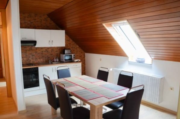 A dining area with a table set for four, a kitchen with a microwave, and a sloped ceiling with a skylight.