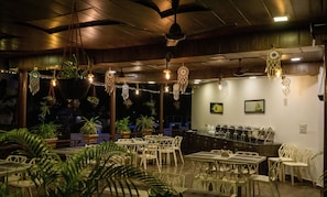 Um restaurante com mesas e cadeiras, apanhadores de sonhos pendurados e luzes de corda.