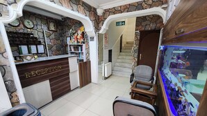 Zona de recepción con pared de piedra, mostrador, escalera y acuario.
