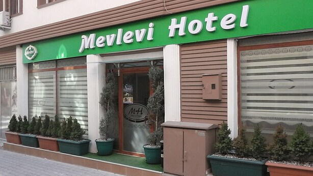 Un hotel llamado 'Merlevi Hotel' con un letrero verde, ventanas amplias y plantas en macetas al frente.
