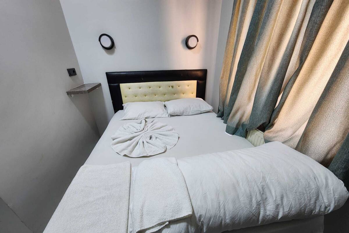 Una cama bien hecha con edredón blanco, cabecera y mesita de noche con lámpara.