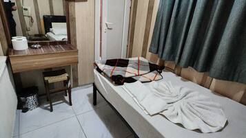 Quarto individual com uma cama, uma escrivaninha, televisão fixada na parede, uma porta e uma cortina.