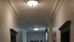 Un pasillo estrecho y tenuemente iluminado, con suelo de baldosas y puertas oscuras a ambos lados.
