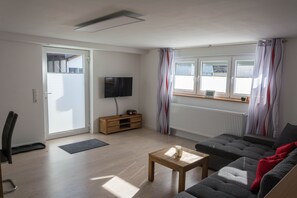 Un salon comprenant un canapé, une table basse, un téléviseur, un meuble en bois et une porte-fenêtre coulissante.