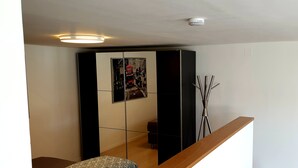 A modern room with a bed, a wooden bench, a small table, a wall-mounted shelf, and a framed picture. - Apartment in a very quiet location, 12 km to Europa Park Rust (Herbolzheim)