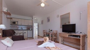 A bedroom with a bed, a TV, a desk, and a kitchenette in the background. - Azahara Playa 23 - Studio (Arona)