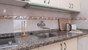 A kitchen with a granite countertop, stainless steel sink, and white cabinets. - Azahara Playa 23 - Studio (Arona)
