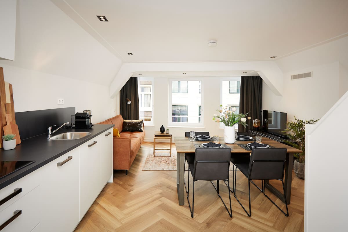 A modern kitchen with a dining area, wooden flooring, and a view of the city through large windows.