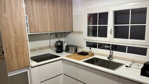 A kitchen with white cabinets, a black countertop, a wooden cutting board, a coffee maker, a toaster, and a window with blinds. - Lighthouse - 3 story holiday home with shared tennis court and sea views (São Martinho do Porto)