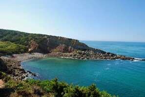 A coastal landscape with rocky cliffs, clear turquoise waters, and lush greenery.