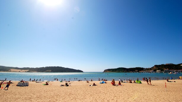 A beach with people sunbathing and swimming, clear skies, and hills in the background. - Lighthouse - 3 story holiday home with shared tennis court and sea views (São Martinho do Porto)