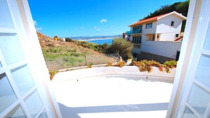 A view from a window overlooking a coastal area with a clear sky, a building with a red roof, and a fenced garden area. - Lighthouse - 3 story holiday home with shared tennis court and sea views (São Martinho do Porto)