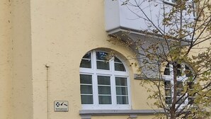 Ein mehrgeschossiges Gebäude mit gelber Fassade, zahlreichen Fenstern und einem Baum davor.