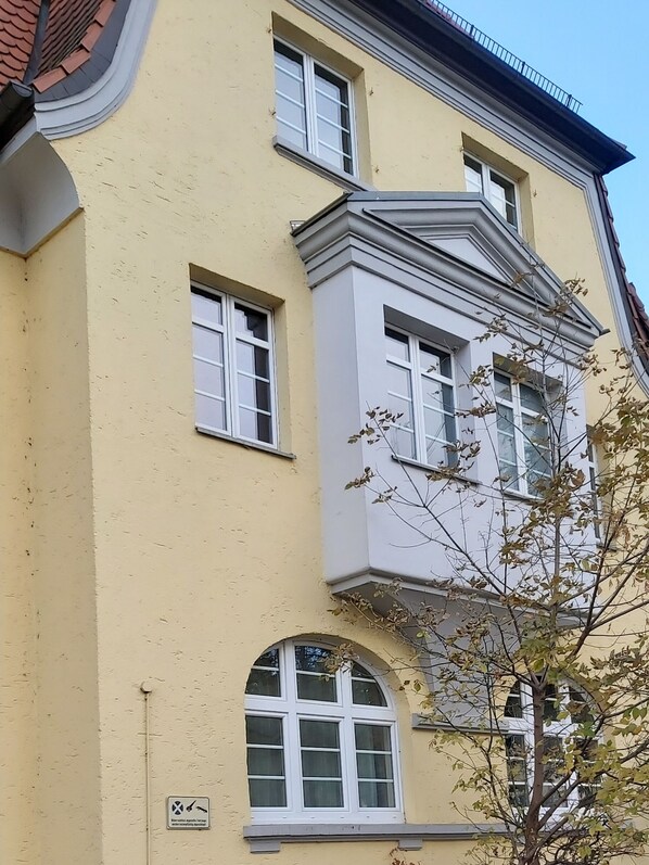 A multi-story building with a yellow facade, multiple windows, and a tree in front.