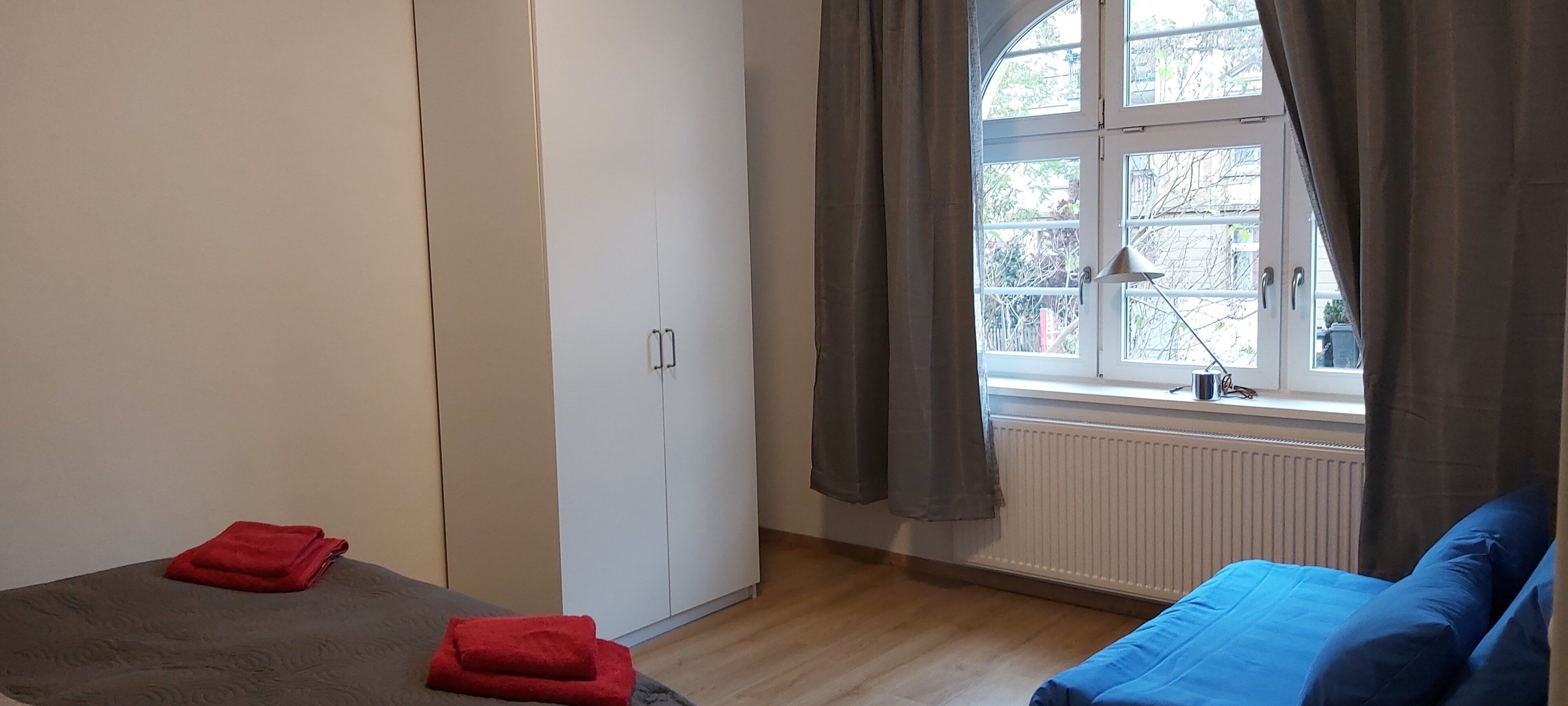 Une chambre à coucher avec un lit, une armoire, une fenêtre avec des rideaux et un radiateur.