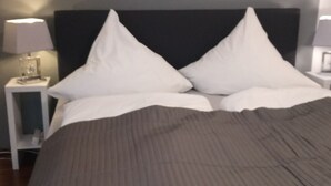 A neatly made bed with a dark headboard, two white pillows, and a grey blanket. There is a small bedside table with a lamp on it. - Fewo Holbeinstr 8 - 2 Schlafzimmer P (Erfurt)