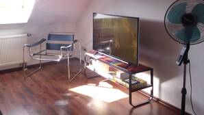 A room with a mirrored TV stand, a standing fan, and a blue and white chair. - Fewo Holbeinstr 8 - 2 Schlafzimmer P (Erfurt)
