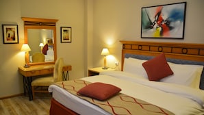 A hotel room with a bed, a desk, a chair, a nightstand, a lamp, a mirror, and a painting on the wall. - The Y Hotel Amman (Amman)