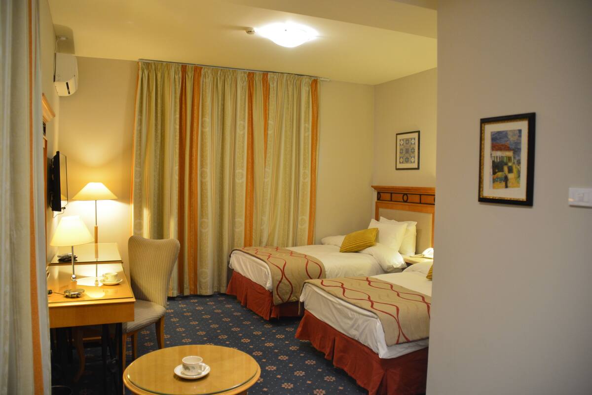 Une chambre d’hôtel avec deux lits, un bureau avec une lampe, une chaise et une petite table ronde avec une tasse.