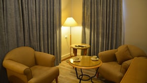 A hotel room with two armchairs, a small round table with a lamp, and a remote control on the table. - The Y Hotel Amman (Amman)