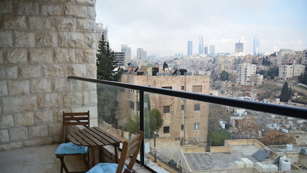 A balcony with a stone wall, a wooden table, and two chairs with cushions. - The Y Hotel Amman (Amman)