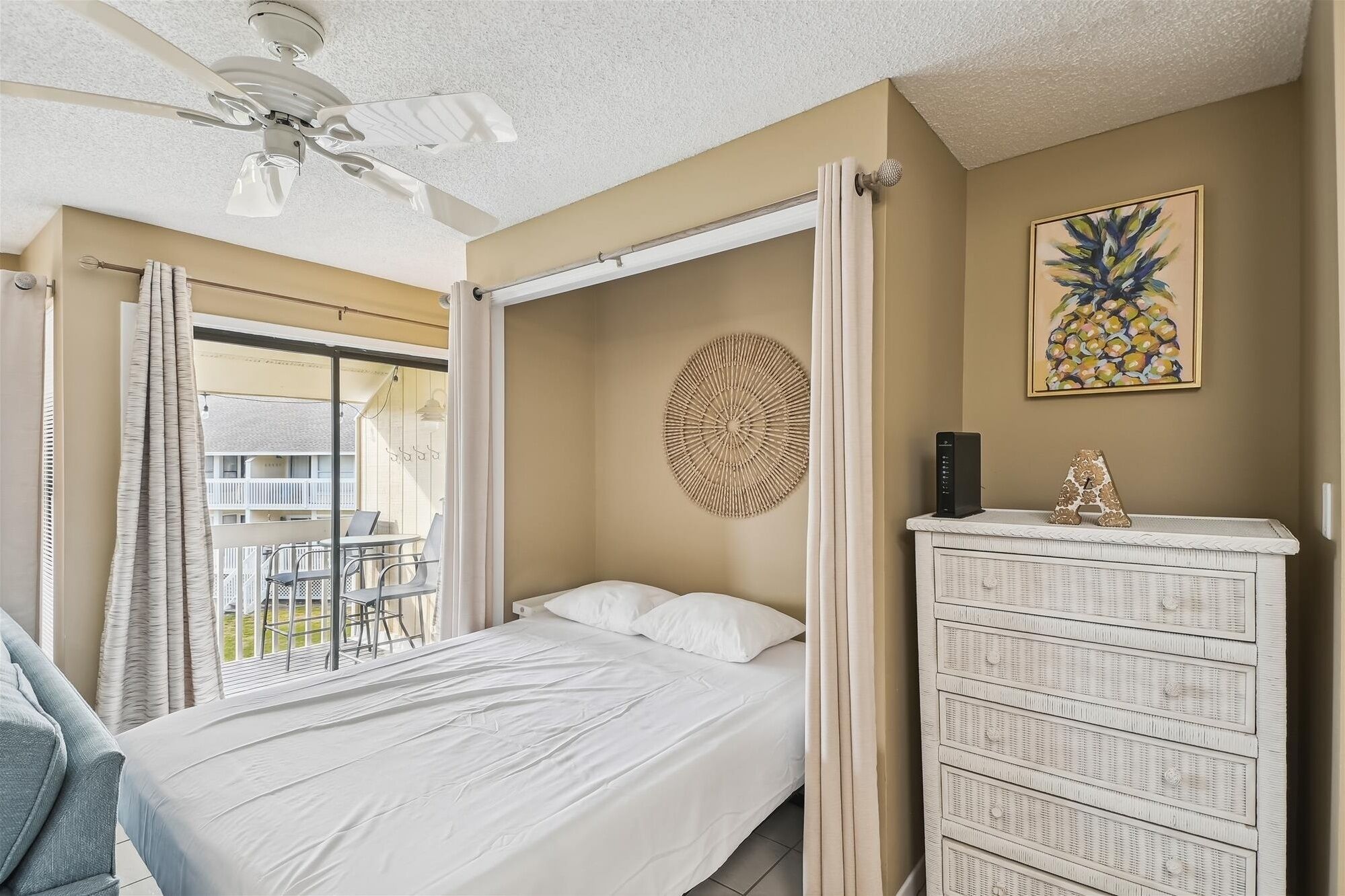 A bedroom with a bed, a ceiling fan, a wall-mounted decorative item, a clock, and a view of the outside balcony.