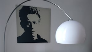 A bedroom with a bed, a wall-mounted lamp, and a poster.