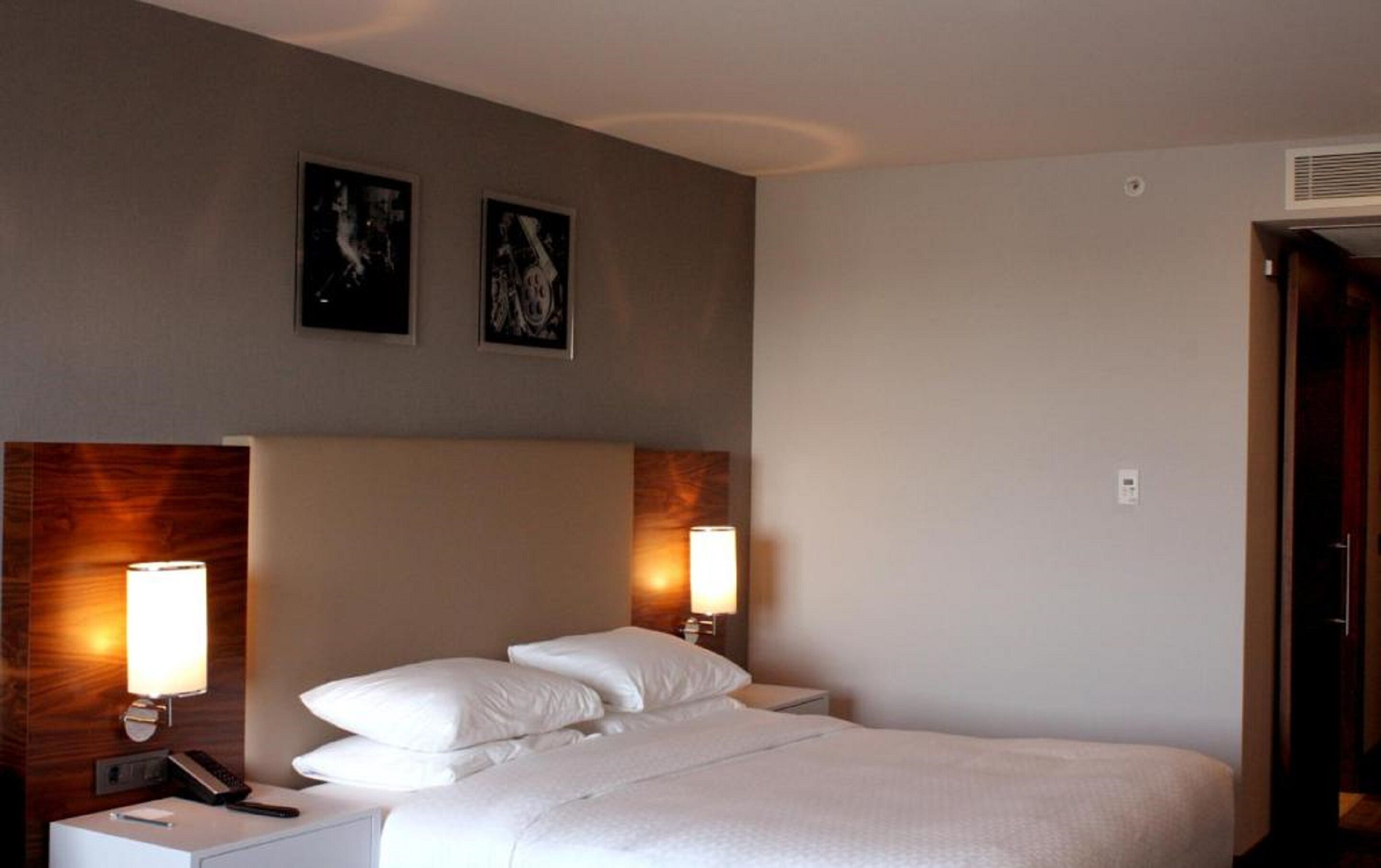 Une chambre d’hôtel avec un grand lit, deux lampes de chevet, une tête de lit en bois et deux tableaux encadrés au mur.