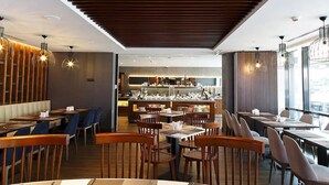 Interior de restaurant modern amb taules i cadires de fusta, il·luminació penjant i una zona de bar central.
