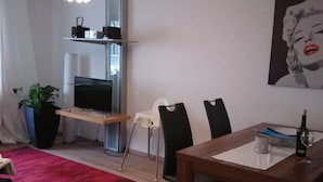 A modern living room with a TV, a fireplace, a dining table with chairs, and a red rug. - Fewo Reißhausstraße 23 - 2 Schlafzimmer (Erfurt)