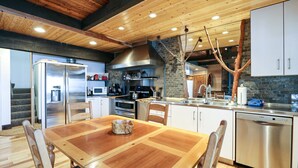 A modern kitchen with wooden ceiling beams, a stone accent wall, stainless steel appliances, and a dining area with a wooden table and chairs. - Bigwood 80 Remodeled, Private Washer Dryer, Close to Eagle Lodge by RedAwning (Mammoth Lakes)