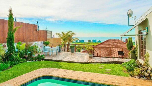 A swimming pool with a tiled deck, surrounded by a grassy lawn and potted plants. - Sun & Sea Apartment (Cape Town)