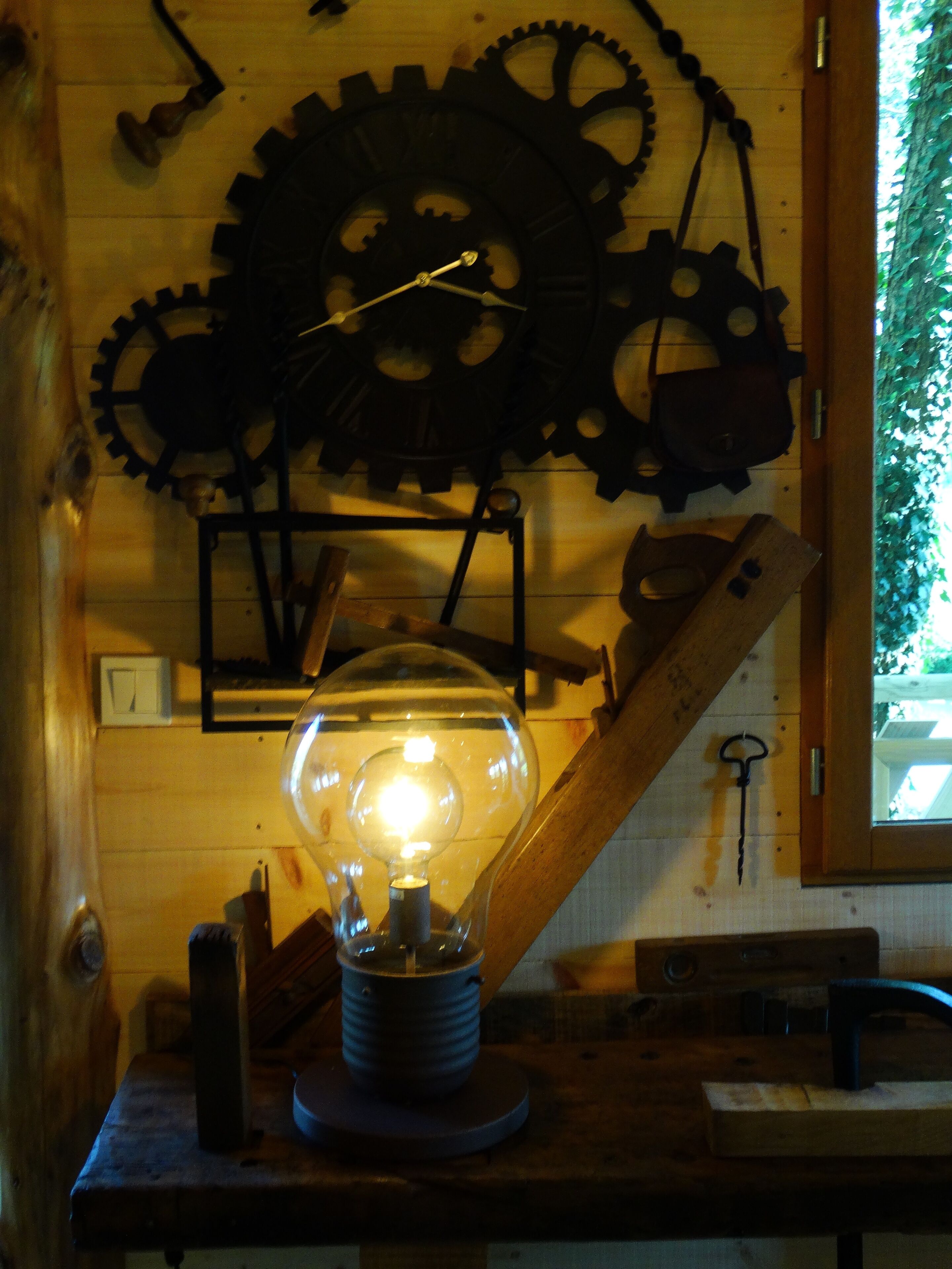 A room with a wooden wall, a large light bulb, and several gears mounted on the wall.